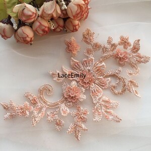 以下が含まれることがあります： ピーチ色の花柄レースアップリケにビーズの装飾が施されています。アップリケは繊細な花柄と複雑なビーズワークが特徴です。