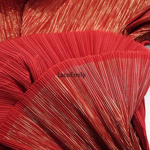 May include: Close-up of red pleated fabric with gold metallic threads. The fabric has a textured, fan-like appearance. The text "LaceEmily" is visible in the lower center of the image. This fabric is suitable for clothing and craft projects.