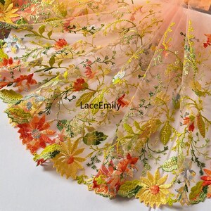 Peut inclure: Tulle brodée de fleurs orange et jaunes avec un effet dégradé. Le tissu a une texture délicate et transparente et présente des motifs floraux complexes.