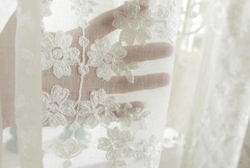 May include: White sheer curtain with delicate floral embroidery. The embroidery is in a white thread and creates a delicate pattern of flowers.