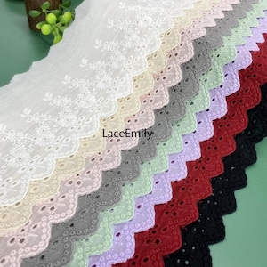 Puede incluir: Una selección de telas de encaje de ojal en varios colores, incluyendo blanco, crema, gris y rojo. La tela tiene un borde festoneado y bordados florales. El texto "LaceEmily" es visible en la tela.