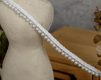 May include: White beaded trim with a delicate lace pattern. The trim features a row of small white pearls along the bottom edge.