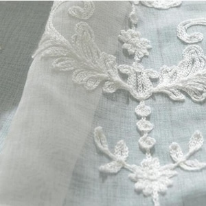May include: White sheer curtain fabric with delicate white embroidered floral designs.