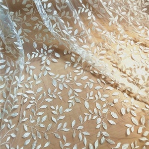 Peut inclure: Tissu blanc transparent avec un motif de feuilles brodées. Le tissu est délicat et a une texture douce et fluide.