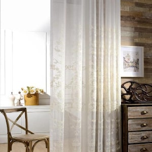 May include: White sheer curtains with an embroidered floral pattern. The curtains are hung on a rod with silver rings.