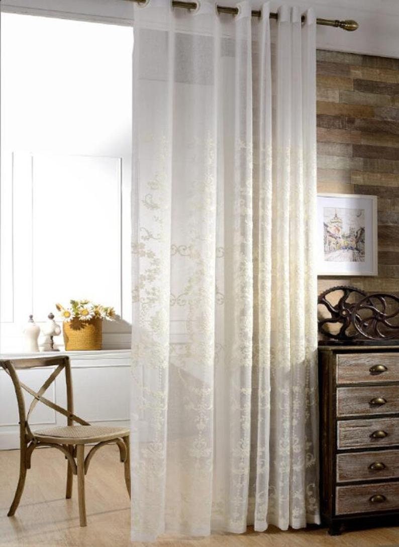 May include: White sheer curtains with an embroidered floral pattern. The curtains are hung on a rod with silver rings.