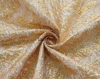 May include: Close-up of gold fabric with a textured, crinkled appearance. The fabric has a metallic sheen and a pattern of raised, irregular shapes. The overall colour is a warm gold with lighter highlights.