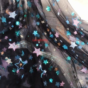 May include: Black sheer fabric with a star pattern and sequins. The stars are in various colors, including blue, pink, and gold. The fabric has a subtle shimmer.