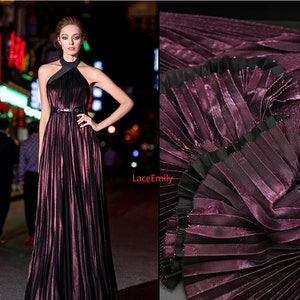 Puede incluir: Un vestido largo, plisado, de color burdeos con un escote halter negro y un cinturón negro. El vestido tiene un acabado brillante y metálico.