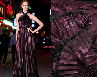 Peut inclure: Une longue robe plissée de couleur bordeaux avec un décolleté halter noir et une ceinture noire. La robe a une finition brillante et métallisée.