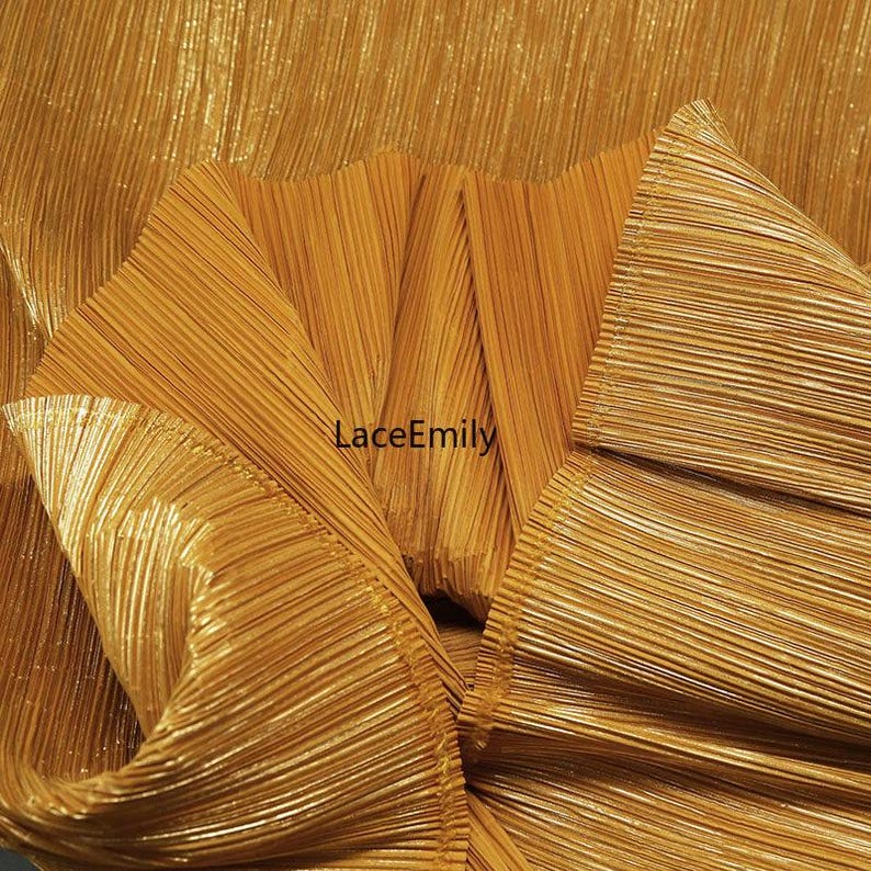 May include: Close-up of a folded, textured fabric in a shimmering gold color. The fabric has vertical pleats and a metallic sheen. The text "LaceEmily" is visible in the center of the image. The fabric appears to be a decorative textile.