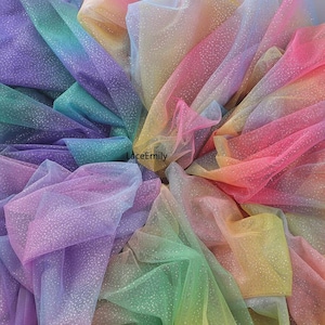 Könnte beinhalten: Nahaufnahme eines Haufens regenbogenfarbenen Tüllstoffs mit einem glitzernden, gesprenkelten Muster. Der Stoff ist eine Mischung aus Farben, darunter Rosa, Gelb, Grün, Blau und Lila. Der Text "LaceEmily" ist sichtbar.