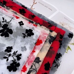 May include: A stack of five sheer fabrics with black floral embroidery. The fabrics are in various colors, including white, red, beige, and gray.
