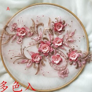 以下が含まれることがあります： 白い背景にピンクとゴールドの刺繍が施された花のアップ。デザインには、パールがあしらわれたピンクの花とゴールドの葉がいくつかあります。