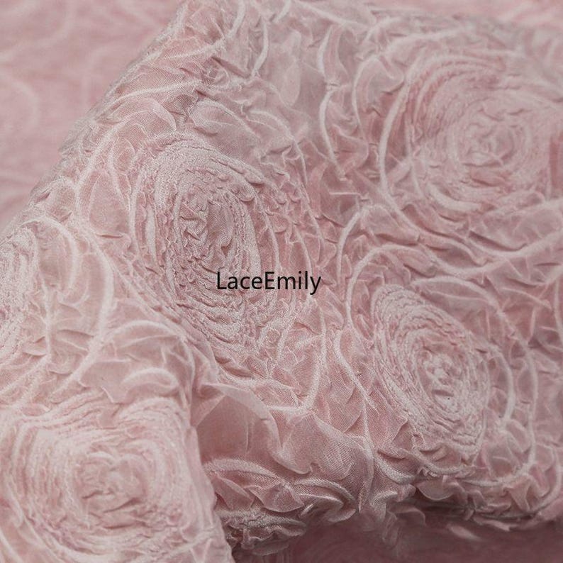 Puede incluir: Primer plano de una tela rosa con un patr&oacute;n floral en relieve. La tela tiene un aspecto texturizado con dise&ntilde;os arremolinados en forma de rosa. El texto "LaceEmily" es visible en la tela. Este material es adecuado para diversos proyectos de artesan&iacute;a y dise&ntilde;o.
