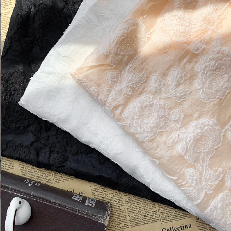 Puede incluir: Tres muestras de tela con un patr&oacute;n floral en relieve. Las muestras son en negro, blanco y melocot&oacute;n.