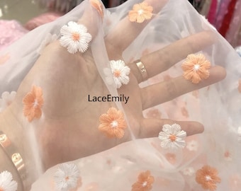 May include: White sheer fabric with embroidered peach and white flowers. The fabric is held in a hand with the text "LaceEmily" printed on it.