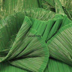 May include: Close-up of a vibrant green pleated fabric. The fabric has a textured, ribbed appearance with vertical lines and a slight sheen. The folds create a layered effect, showcasing the material's depth and texture. The text "LaceEmily" is visible.