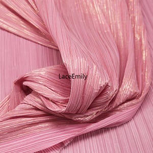 May include: Close-up of a pink pleated fabric with a metallic sheen. The fabric is gathered and draped, creating soft folds and shadows. The text "LaceEmily" is visible on the fabric.