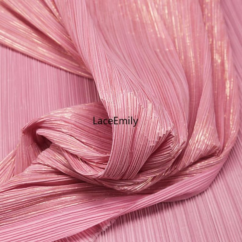 May include: Close-up of a pink pleated fabric with a metallic sheen. The fabric is gathered and draped, creating soft folds and shadows. The text "LaceEmily" is visible on the fabric.