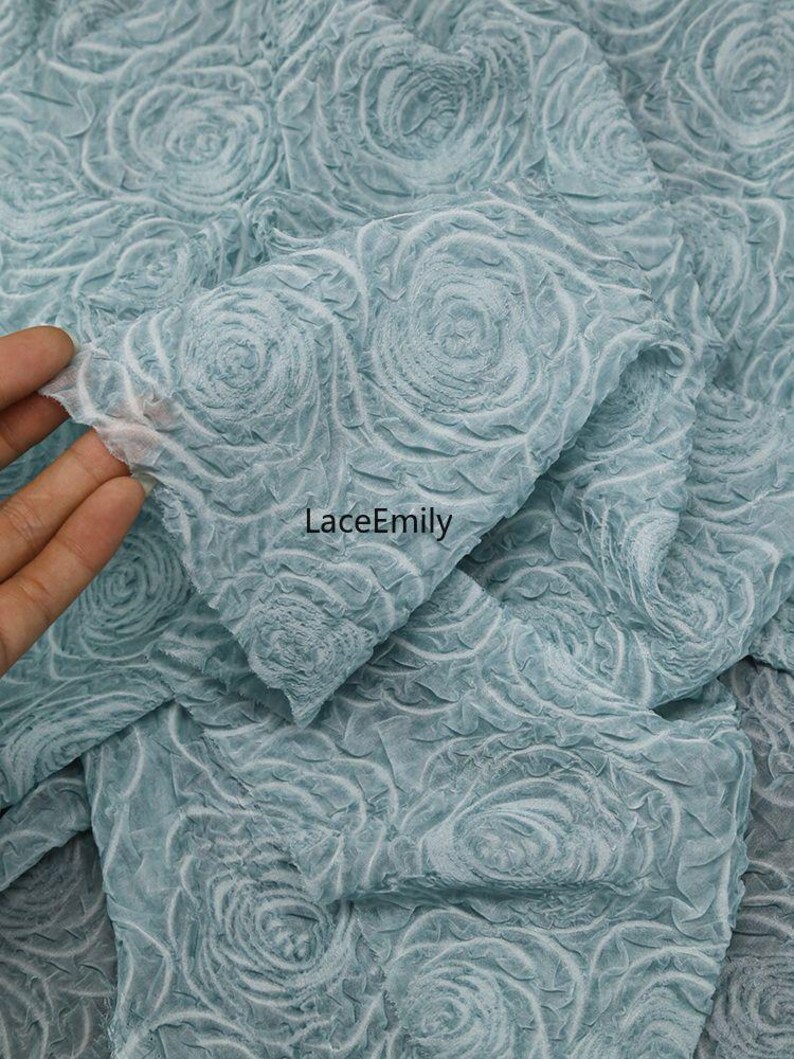 Puede incluir: Primer plano de una tela azul claro con un patr&oacute;n de rosas en 3D. La tela es suave y texturizada, con una calidad delicada y casi transparente. El texto "LaceEmily" es visible.