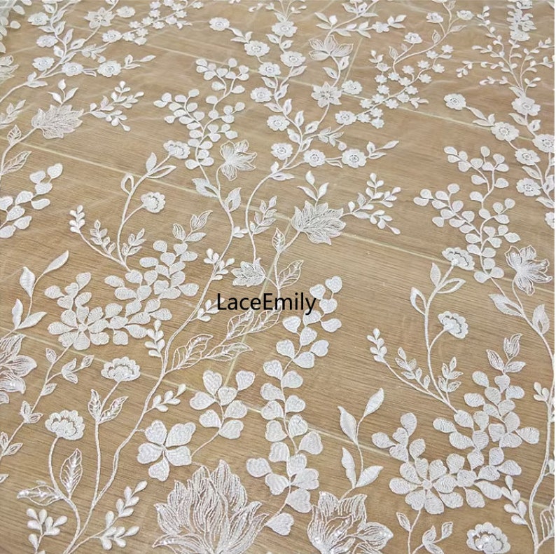 Pu&ograve; includere: Tessuto di pizzo floreale bianco con un delicato motivo di fiori e foglie. Il tessuto &egrave; leggero e trasparente, perfetto per creare abiti, accessori o decorazioni per la casa.