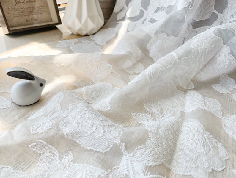 Puede incluir: Tela blanca transparente con un patr&oacute;n floral en relieve. La tela es delicada y tiene una textura suave y fluida.