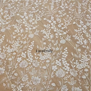 Pu&ograve; includere: Tessuto di pizzo floreale bianco con un delicato motivo di fiori e foglie. Il pizzo &egrave; su uno sfondo beige. Il testo "LaceEmily" &egrave; visibile al centro dell'immagine.