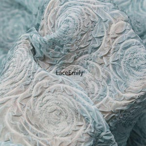 Puede incluir: Primer plano de una tela azul claro con un patr&oacute;n floral arremolinado texturizado. La tela tiene un efecto en capas y tridimensional, con el texto "LaceEmily" visible en el centro inferior.