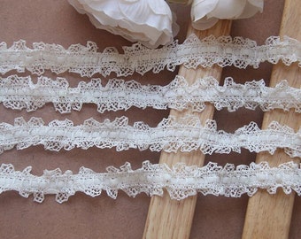 May include: White lace trim with a ruffled edge and a row of small white beads. The trim is shown on a wooden surface.