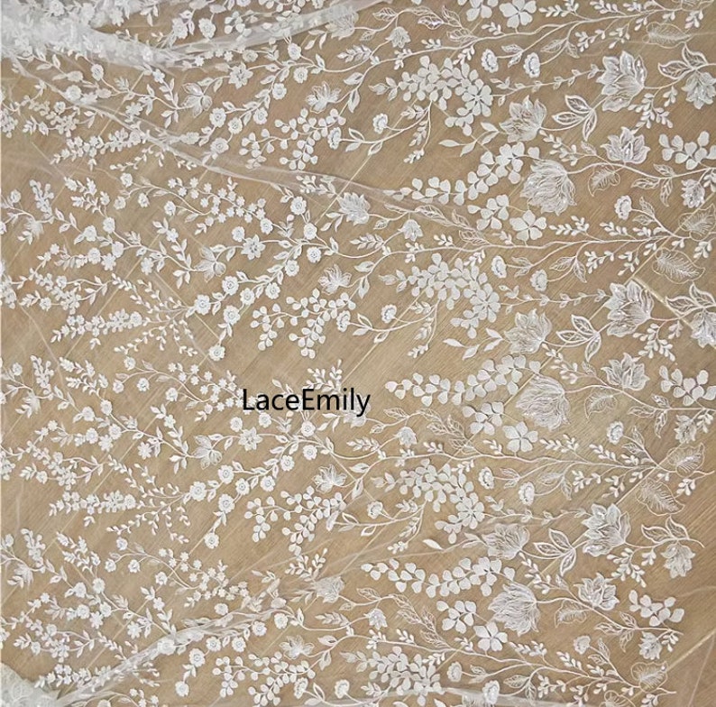 Pu&ograve; includere: Tessuto di pizzo floreale bianco con un delicato motivo di fiori e foglie. Il tessuto &egrave; trasparente e ha una texture morbida e fluida. Il testo "LaceEmily" &egrave; visibile al centro dell'immagine.