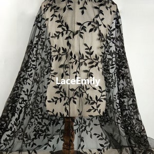 Könnte beinhalten: Schwarzer, durchsichtiger Stoff mit einem zarten floralen Stickmuster. Die Stickerei zeigt schwarze Blätter und Ranken auf einem schwarzen Netzstoff. Der Stoff ist leicht und durchscheinend, wodurch er sich ideal für die Herstellung von Kleidungsstücken und Accessoires eignet.