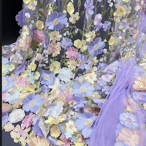 May include: Purple tulle fabric with embroidered flowers in shades of pink, yellow, and blue. The flowers are 3D and have a delicate, feminine look. The fabric is perfect for making dresses, skirts, and other garments.