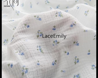 May include: White fabric with a delicate floral pattern of small blue flowers and green leaves. The fabric has a textured, slightly wrinkled appearance. The text "LaceEmily" is visible on the fabric.