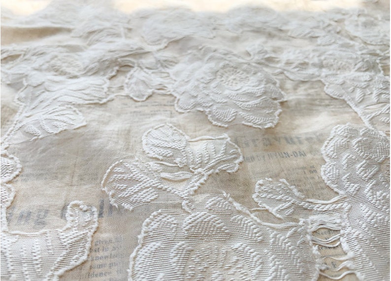 Puede incluir: Tela blanca bordada con un patr&oacute;n floral. La tela es transparente y delicada, con un dise&ntilde;o en relieve.