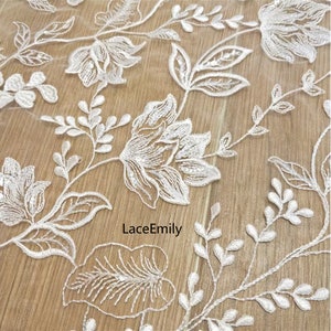 Pu&ograve; includere: Tessuto di pizzo floreale bianco con un delicato motivo di fiori e foglie. Il tessuto &egrave; leggero e trasparente, perfetto per progetti di artigianato, abbigliamento e arredamento.