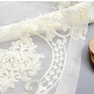 May include: White sheer curtain panel with an embroidered floral design. The embroidery is in a cream color and features a repeating pattern of stylized flowers and leaves.