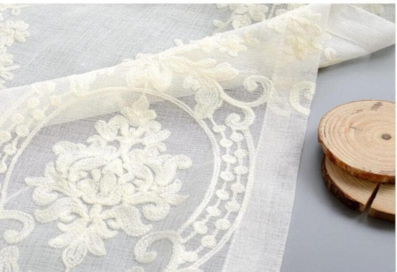 May include: White sheer curtain panel with an embroidered floral design. The embroidery is in a cream color and features a repeating pattern of stylized flowers and leaves.