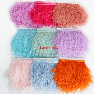 May include: A collection of colorful ostrich feather fringe in various shades, including pink, red, orange, blue, and purple. The fringe is attached to a white ribbon base, perfect for crafting and embellishments. The text "LaceEmily" is visible.