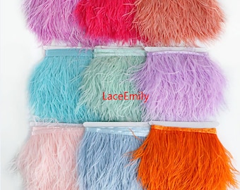 May include: A collection of colorful ostrich feather fringe in various shades, including pink, red, orange, blue, and purple. The fringe is attached to a white ribbon base, perfect for crafting and embellishments. The text "LaceEmily" is visible.