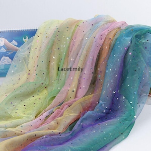 Könnte beinhalten: Regenbogen-Tüllstoff mit silbernen Glitzersternen und -monden. Der Stoff ist gefaltet, um die verschiedenen Farben des Regenbogens zu zeigen.