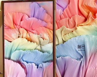 Peut inclure: Un tissu plissé à dégradé arc-en-ciel avec le texte "初-设计师面料" en blanc. Le tissu est plié et drapé de manière à créer un motif ondulé.