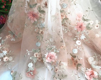 May include: Peach-colored tulle fabric with embroidered floral designs. The fabric features 3D flowers in shades of pink and white.