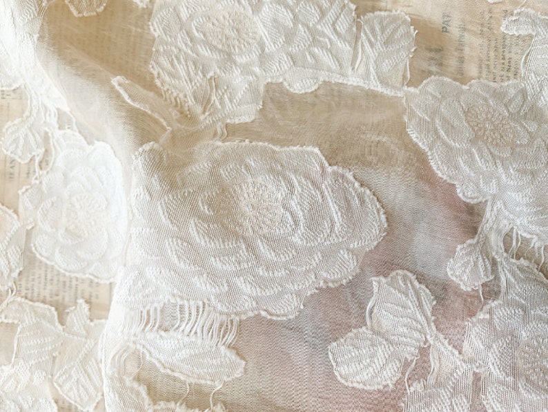 Puede incluir: Tela de encaje floral blanca con un delicado patr&oacute;n bordado. La tela es transparente y tiene una textura suave y fluida.