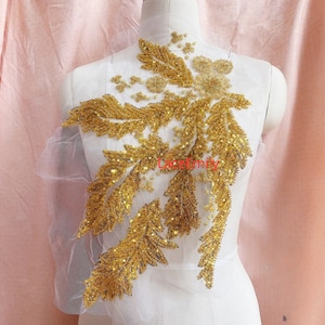 May include: Gold sequined applique with a leaf design. The applique is on a white background.