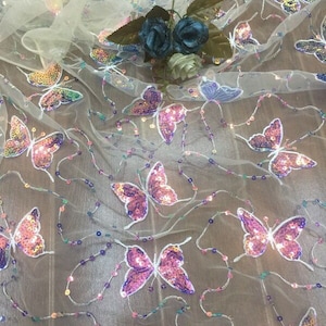 May include: White sheer fabric with iridescent sequins in the shape of butterflies. The butterflies are pink, purple, and blue.