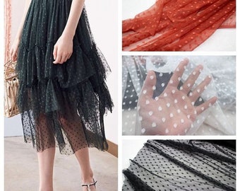 May include: A green tulle skirt with white polka dots. The skirt is layered and has a ruffled hem. The skirt is shown on a model wearing sandals.