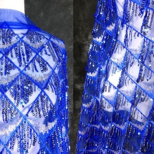 Op de afbeelding: Blauw paillettenstof met franjes. De stof heeft een ruitpatroon en is gemaakt van een transparant gaasmateriaal.