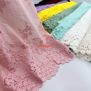 May include: A collection of embroidered lace fabric in various colors, including pink, yellow, green, blue, and white. The fabric has a delicate floral design and a scalloped edge.