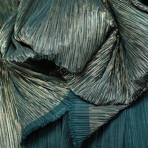 May include: Close-up of teal fabric with vertical pleats and a metallic gold sheen. The fabric is gathered and folded, creating a textured and layered effect. The material has a luxurious appearance, suitable for apparel or decorative projects.